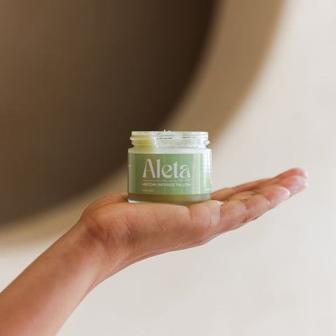 Hand holding a jar of Aleta cream against a neutral background