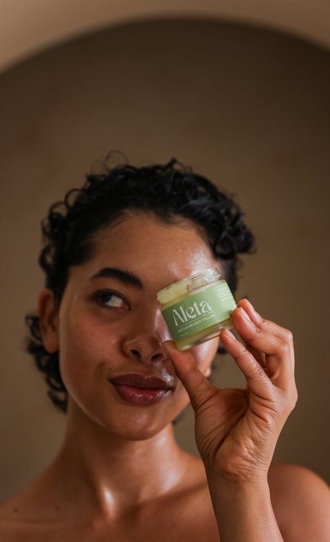 Woman holding a jar of Aleta skincare product near her face against a neutral background